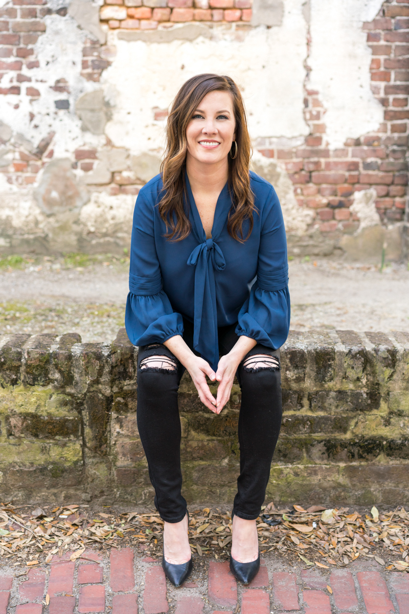 Headshot of a woman entrepreneur sitting on a brick wall