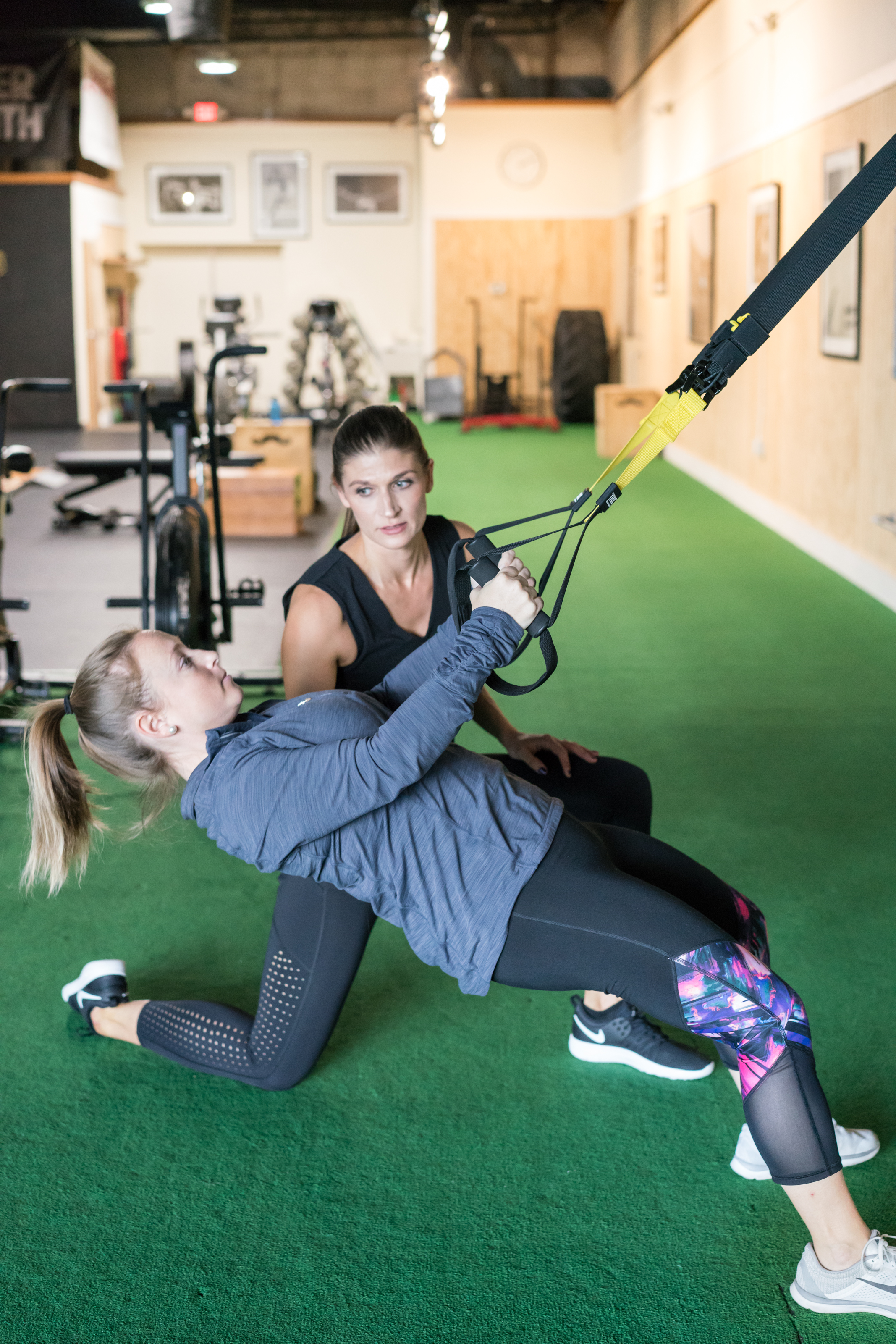 A personal trainer and client working out in a gym with TRX