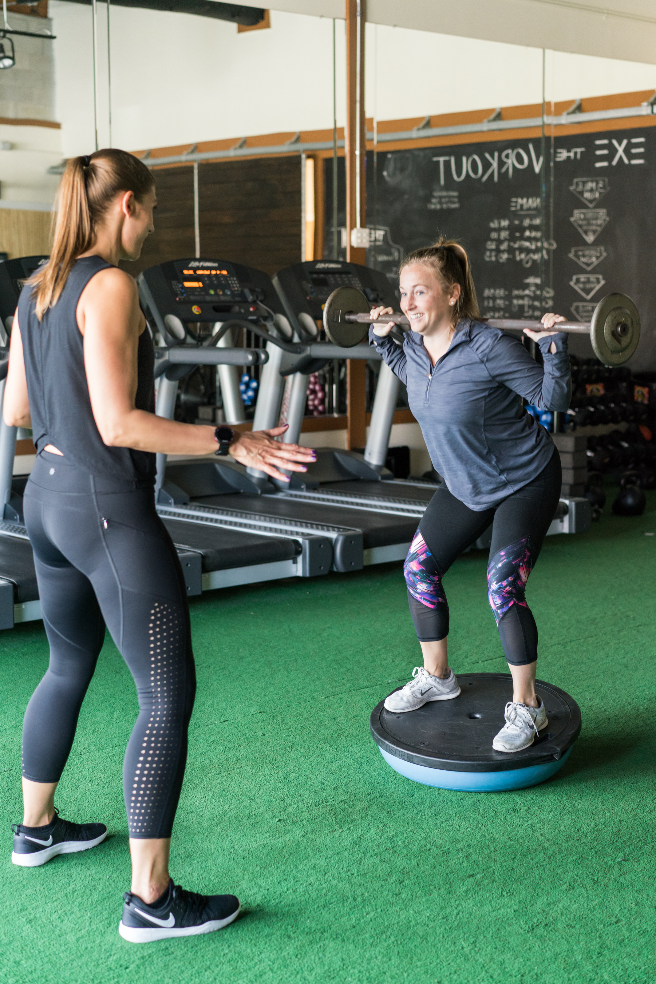 A personal trainer encouraging a client balancing and holding a weight behind her shoulders