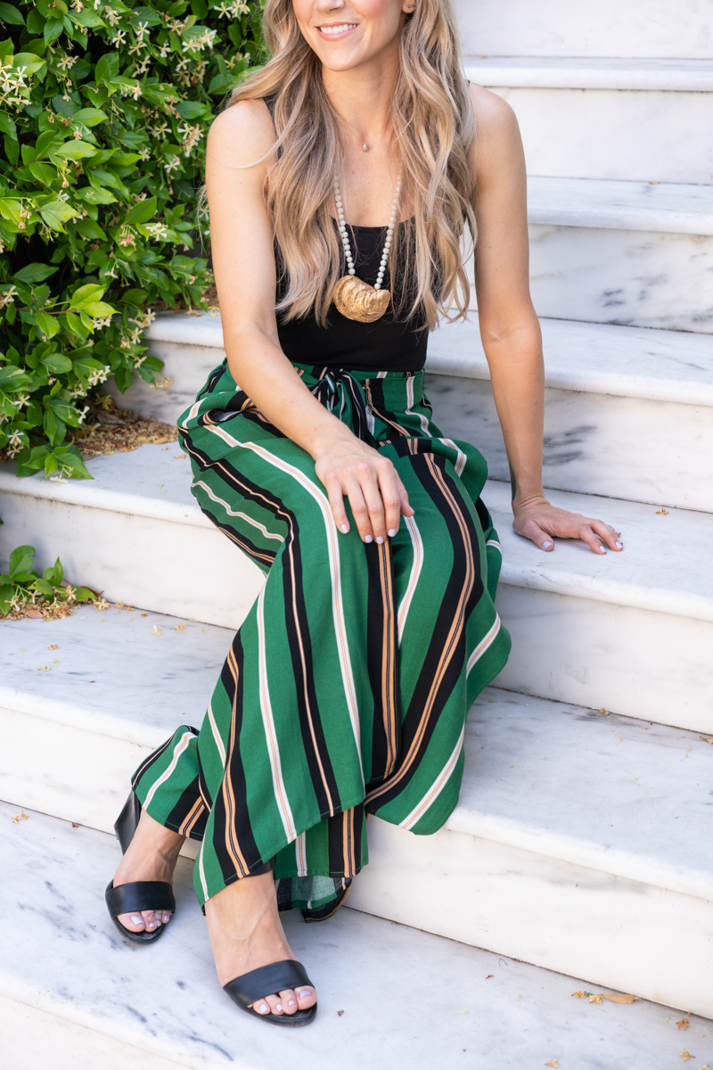 Detail shot of a fashion blogger's outfit (striped green pants and a black tank top)