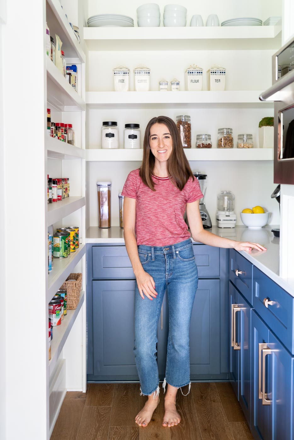 Woman standing in an organized pantry with white shelves and blue cabinets