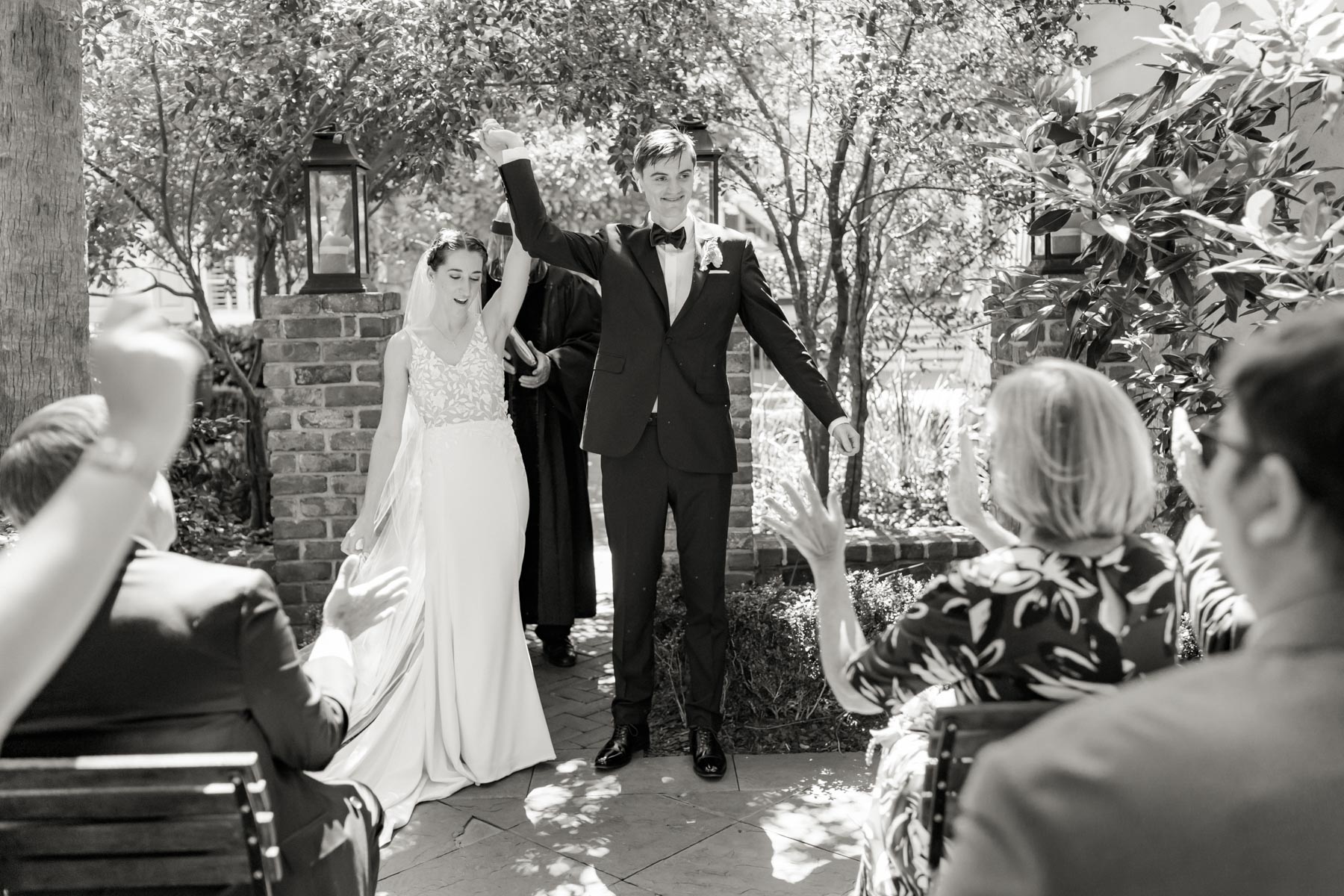 A bride and groom hold their hands up in celebration before they walk down the aisle as husband and wife