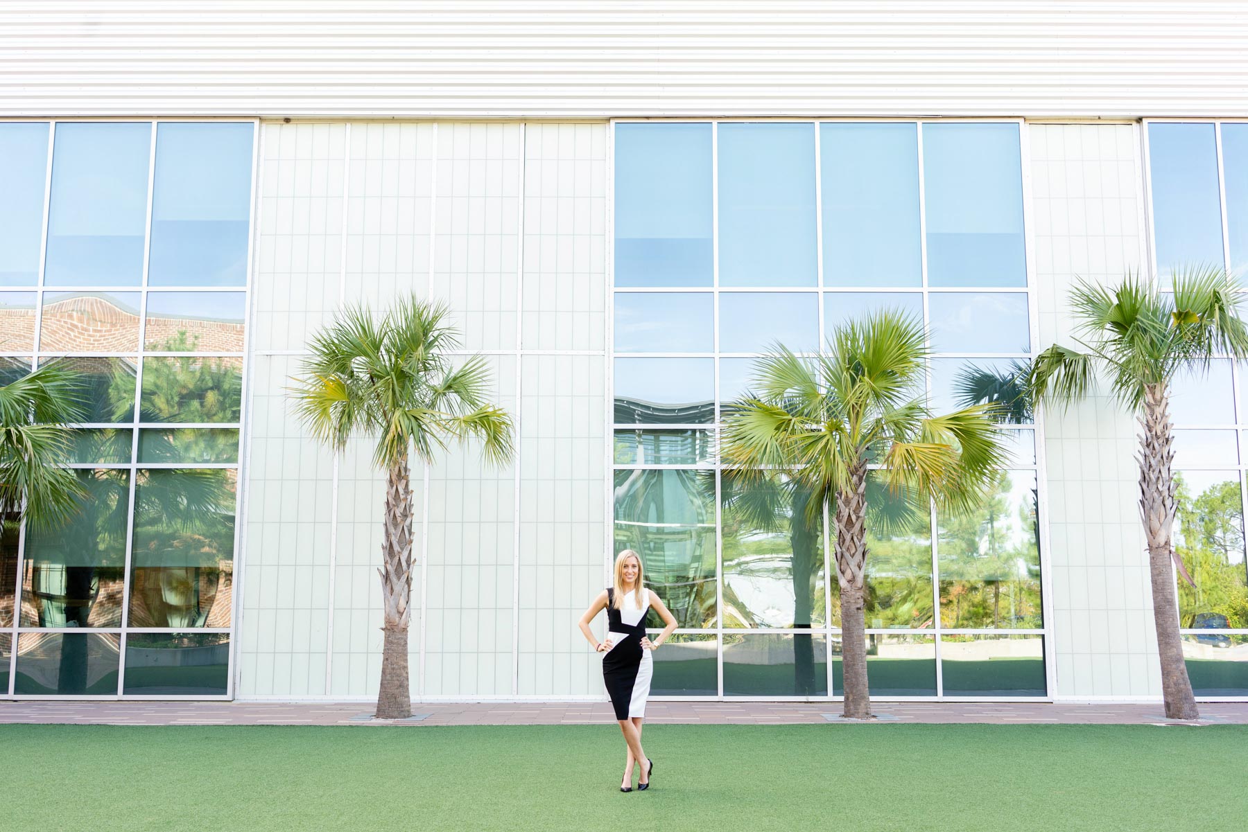Business portrait of a woman in a black and white dress standing in front of a modern office building with palm trees