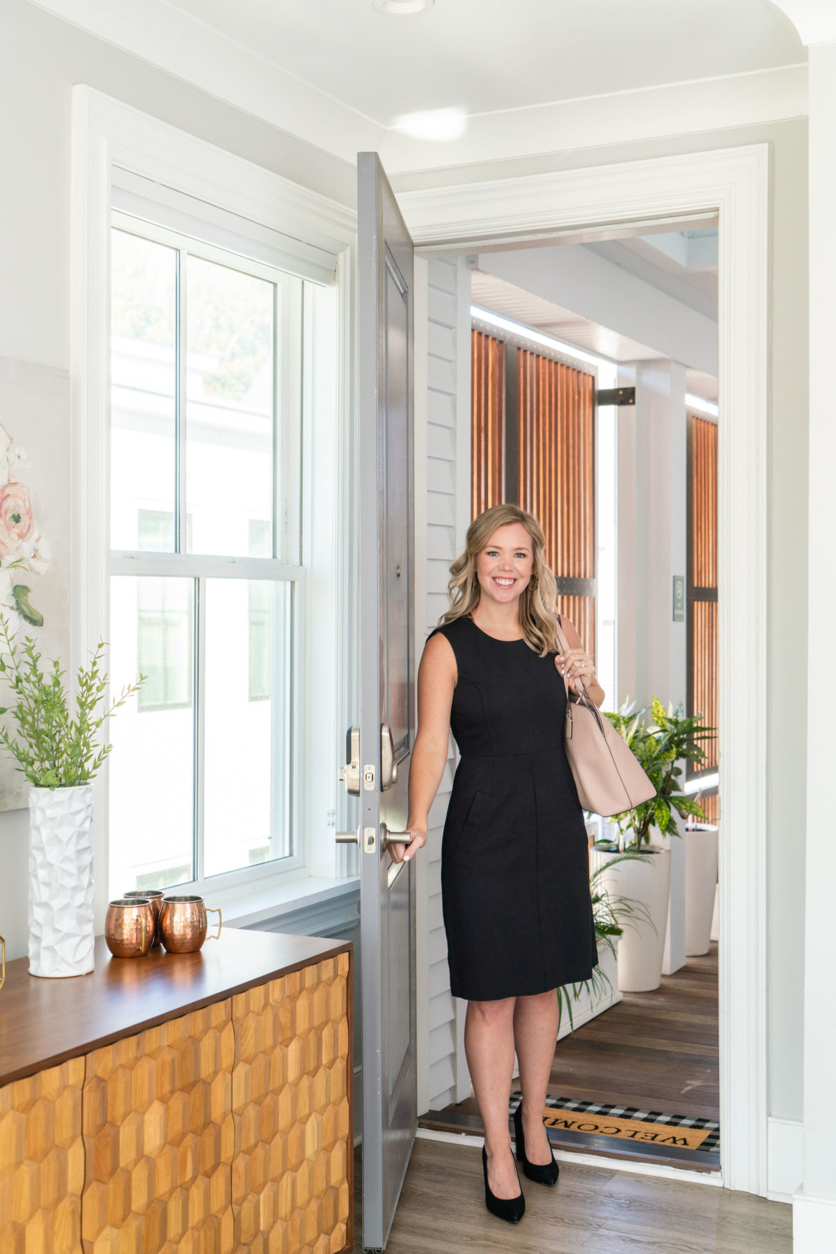 A brand photo of a realtor in Charleston, South Carolina. She is walking through the front door of a property wearing a black dress and a handbag. 