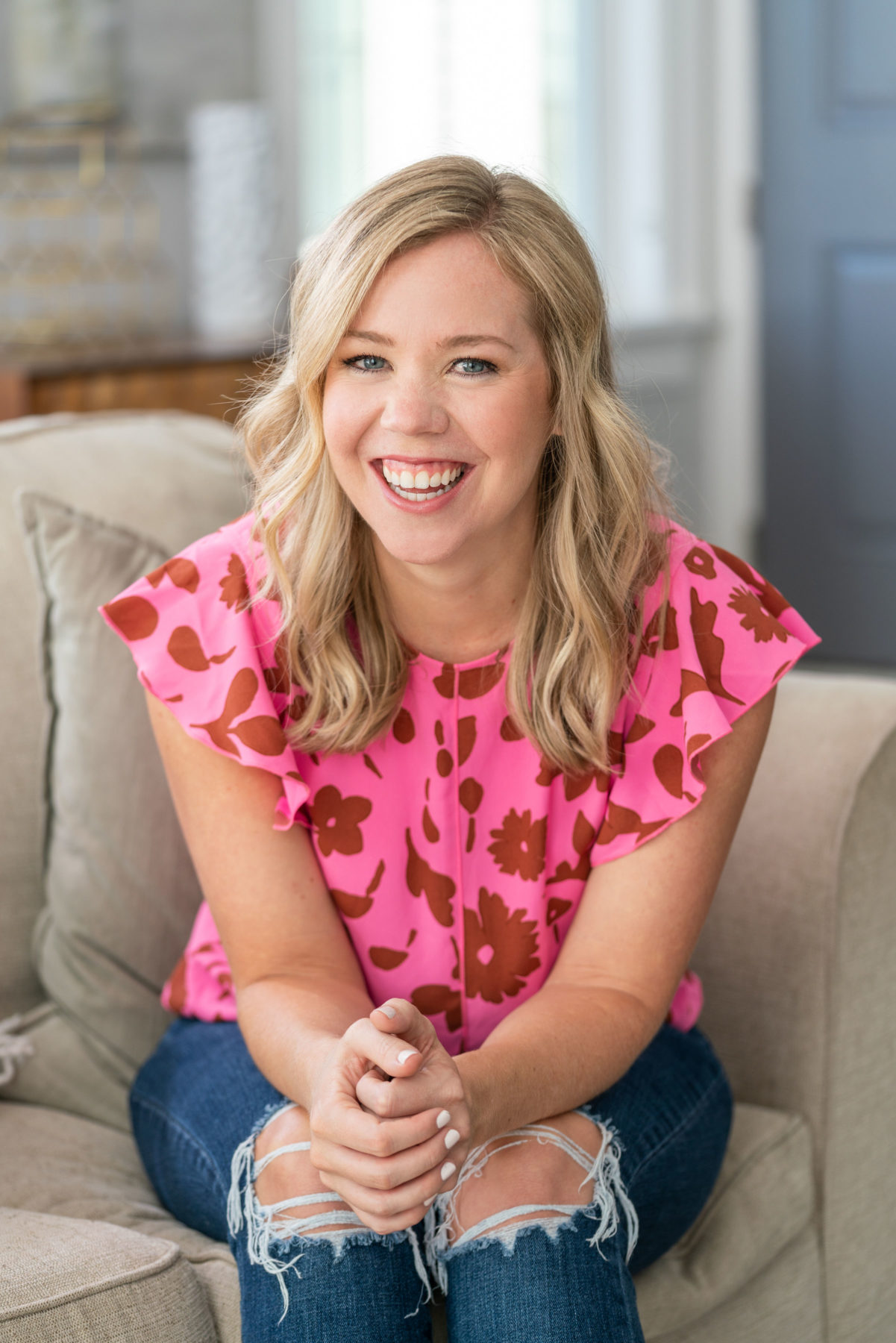 A personal branding portrait of a realtor. She is wearing a casual outfit for her brand photoshoot, a bright pink top patterned with flowers, and ripped jeans. 
