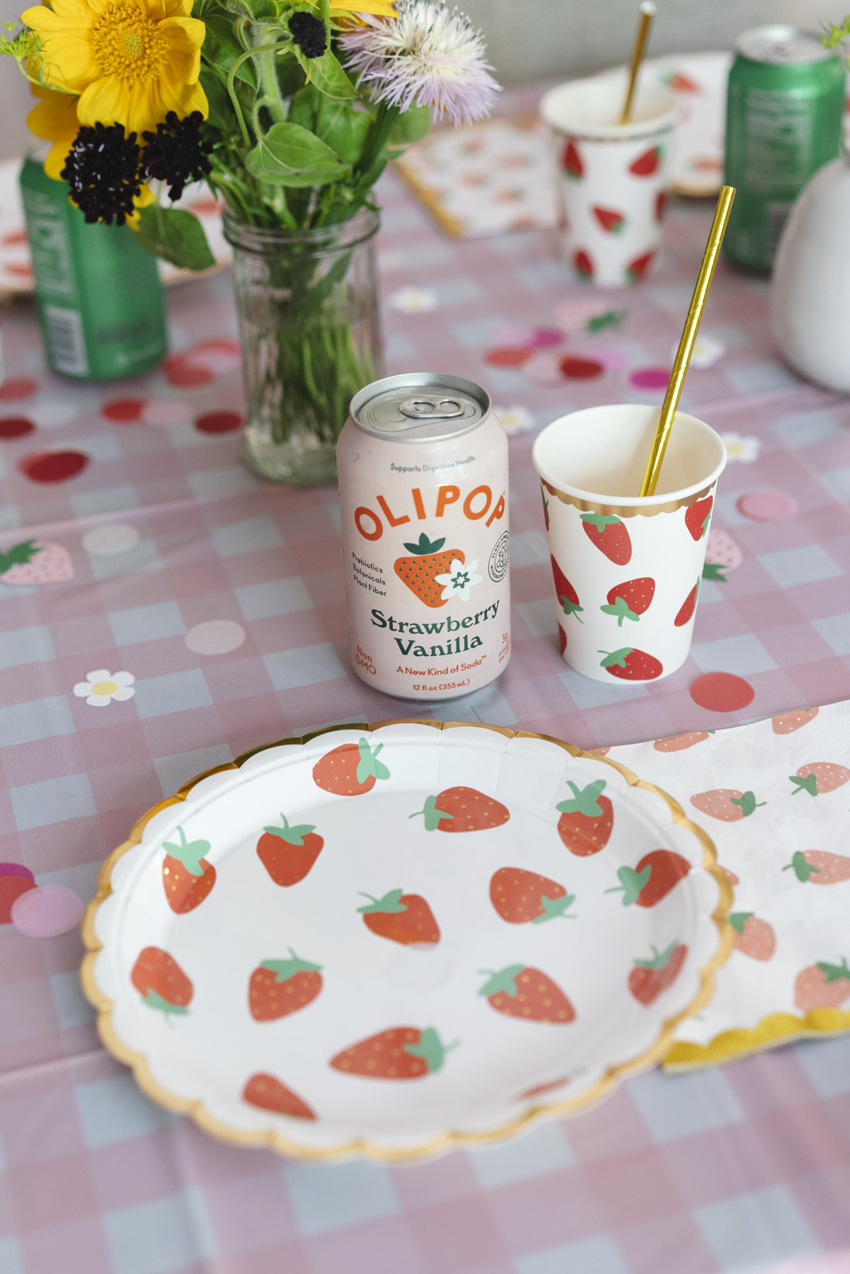 Close up of a strawberry patterned paper plate and cup and a can of strawberry vanilla Olipop. 