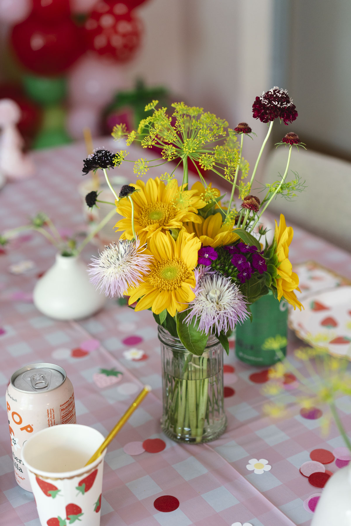Close up of the vase of flowers on the table. Flowers are yellow and green, with a touch of purple. 