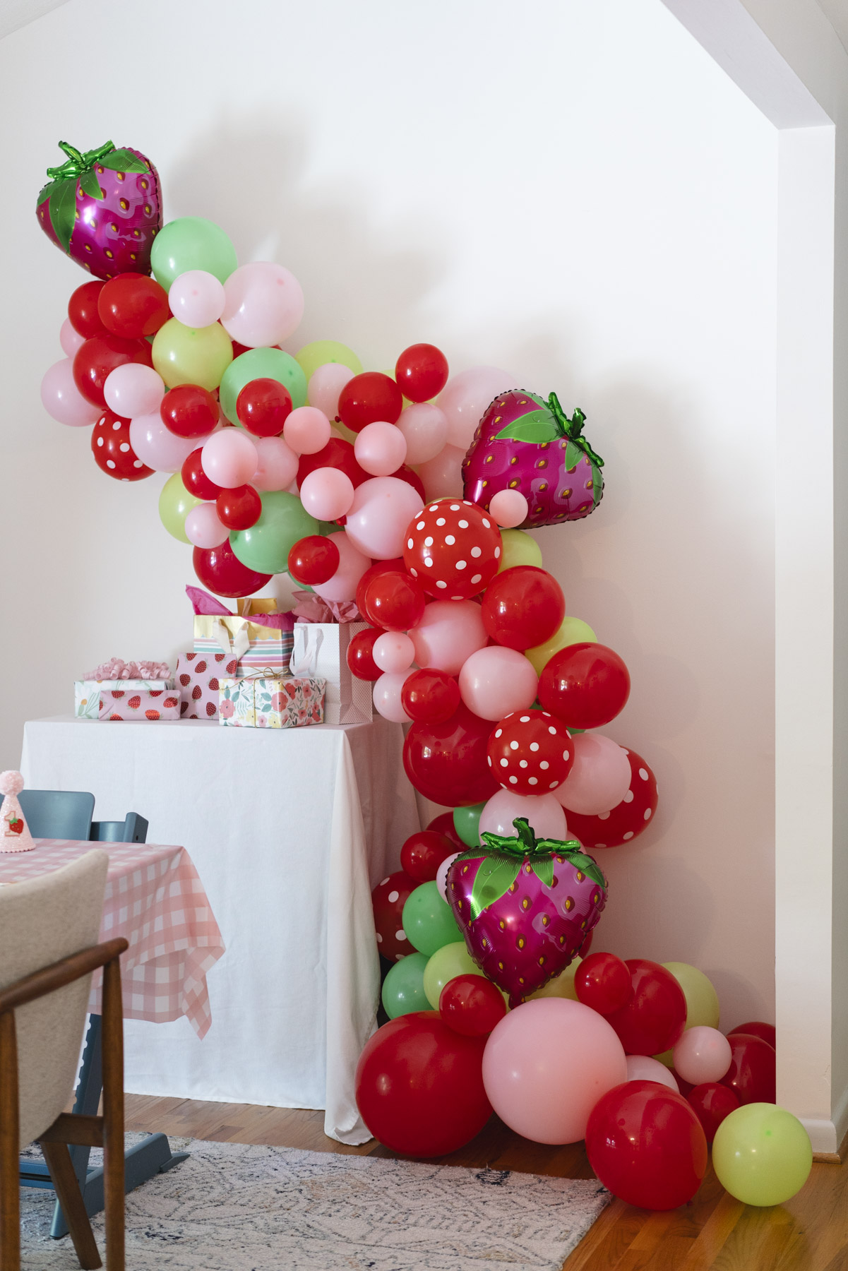 Pink and red strawberry ballon arch flowing next to a table of birthday presents. 