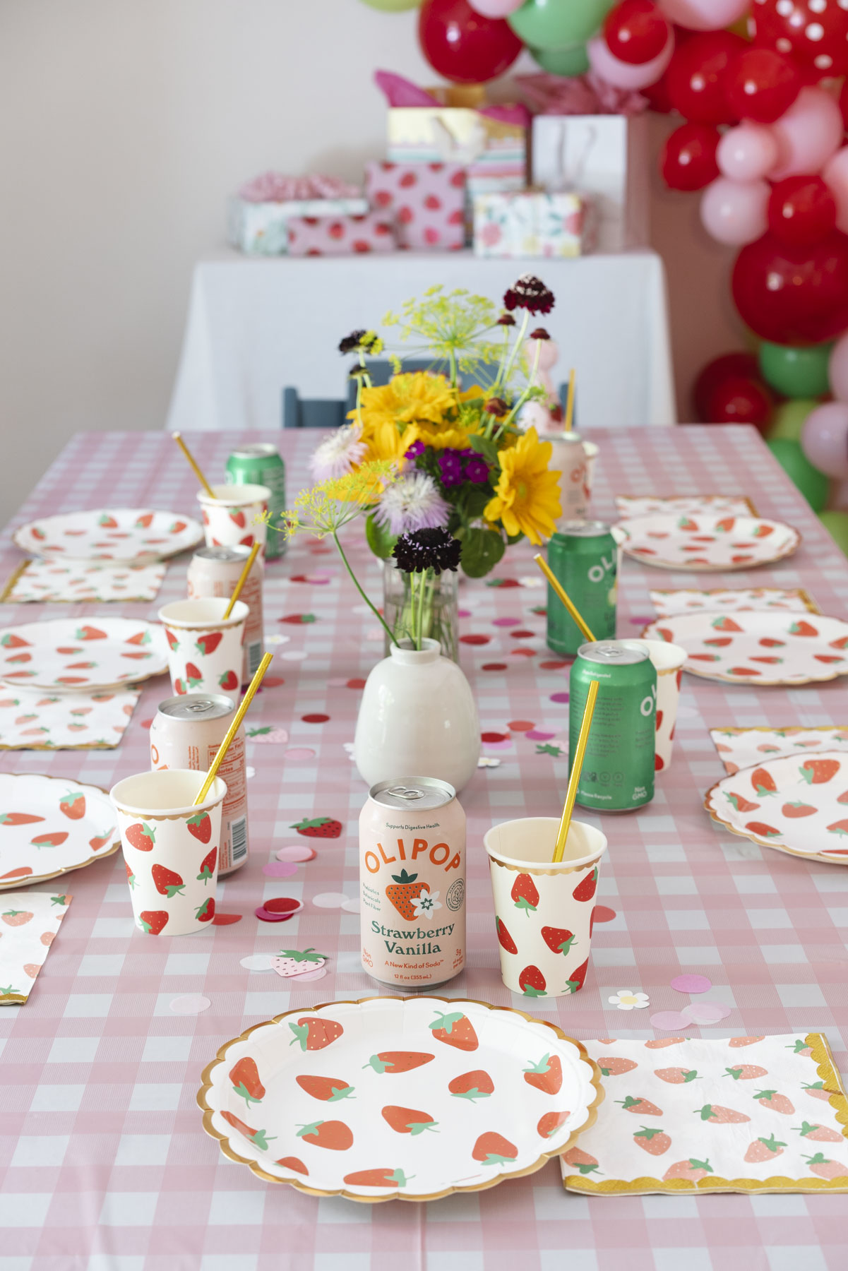 Close up of the strawberry plates, cups, and napkins on the pink and white gingham table cloth. 
