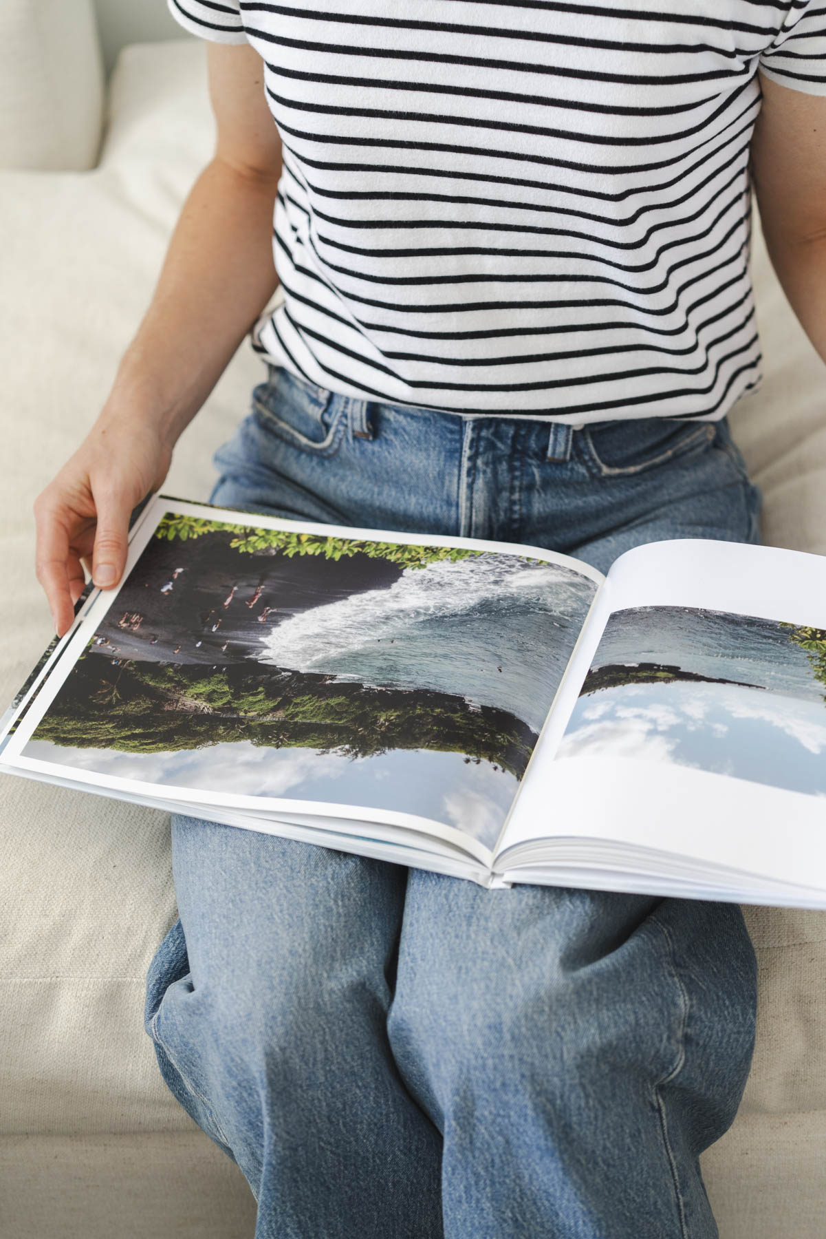 Abby holding one of the photo books on her lap and reading it. She is wearing jeans and a striped tee. 