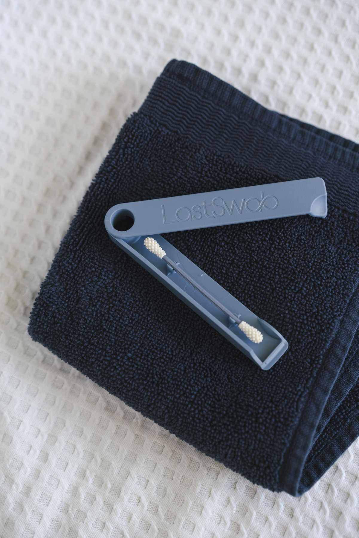 Flat lay photo of the Last Swab sitting on top of a navy blue hand towel that is on top of a white, waffle textured towel. 