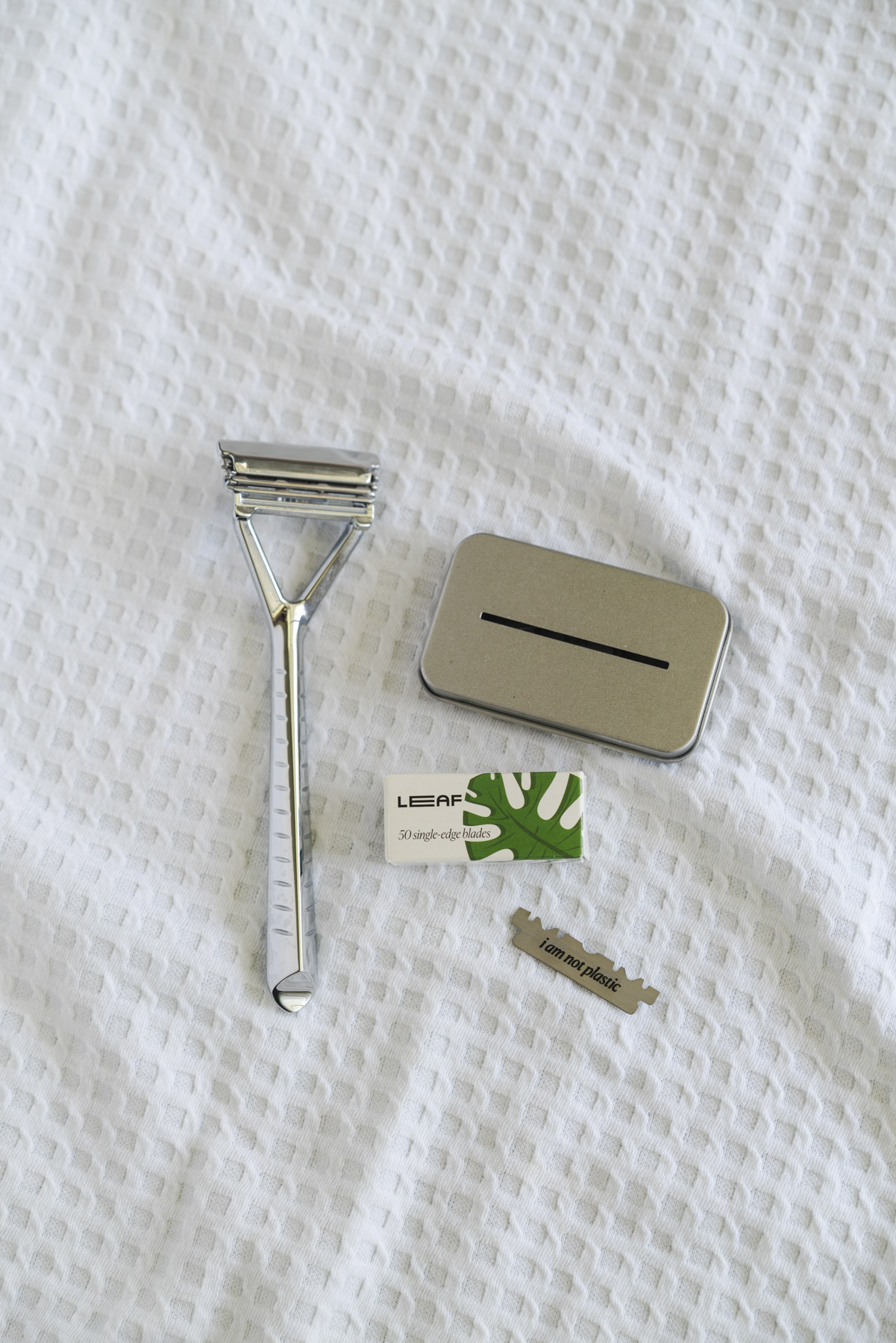 Flat lay photo of the LEAF razor and case of refills on top of a white, waffle textured towel. 