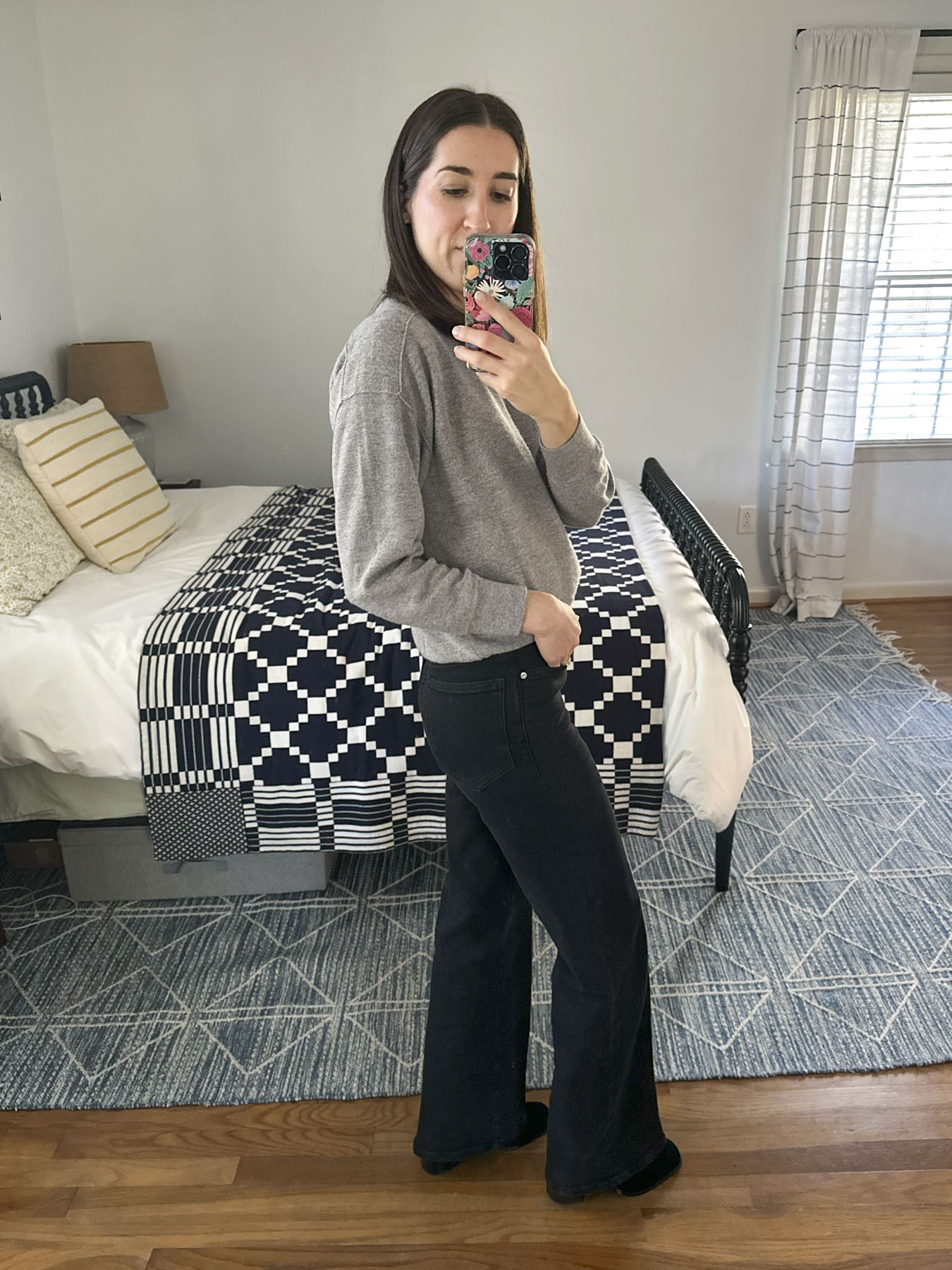 Abby taking a mirror selfie wearing the black wide leg jeans and a grey top.