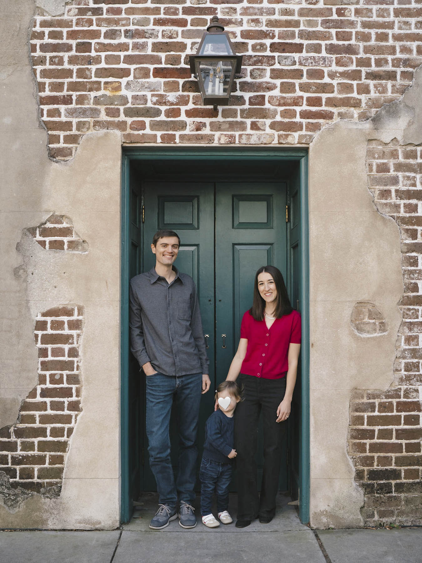 Abby and her husband and daughter posing in front of a green door.