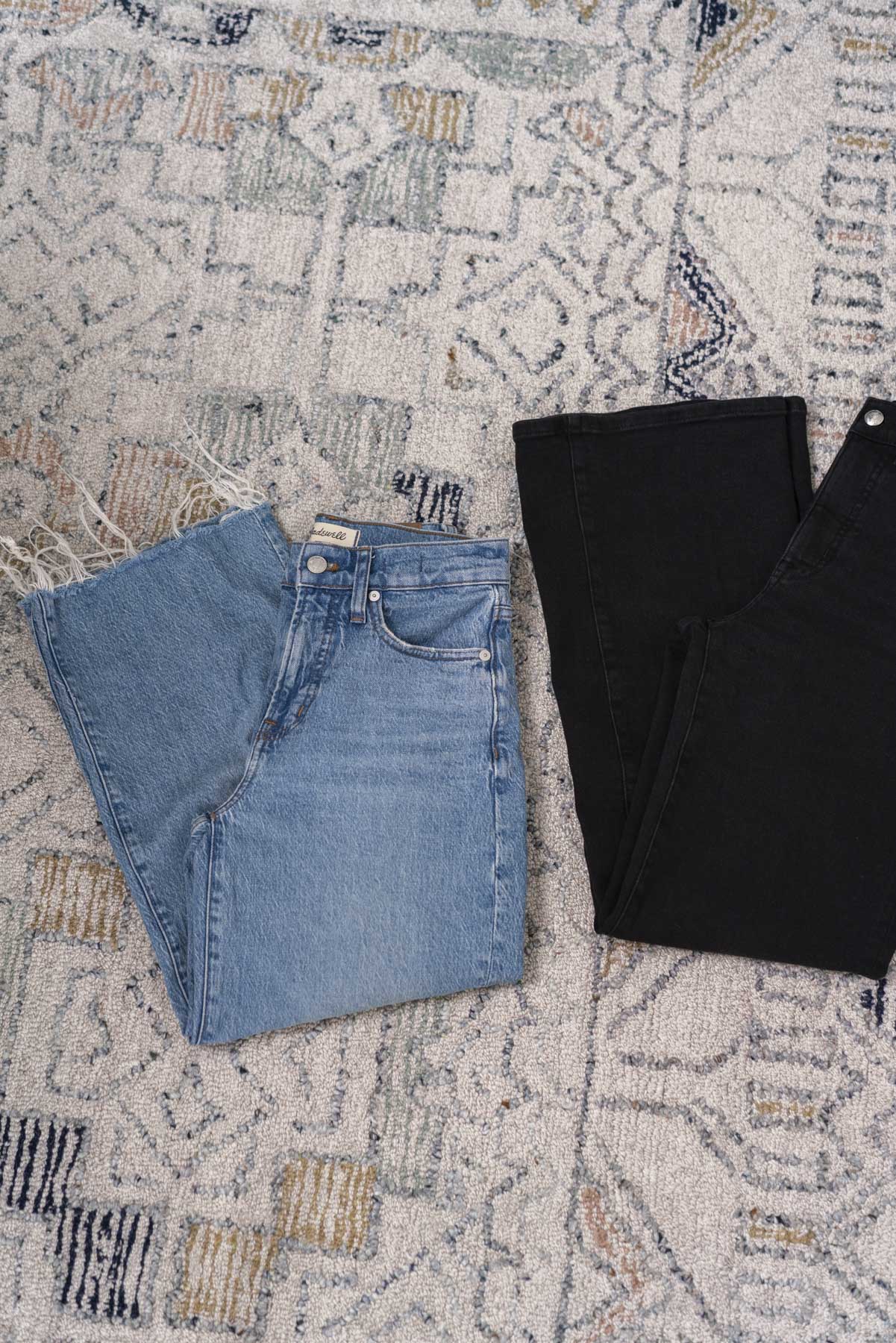 Flat view of two pairs of jeans folded. One pair is blue, the other is black.
