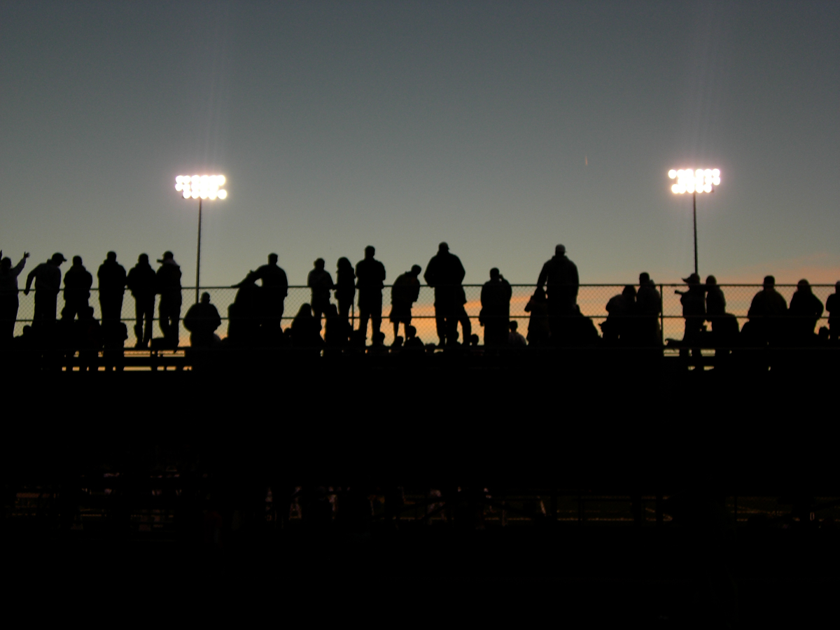 High school football fans silhouetted against a sunset