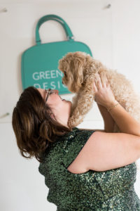 Woman entrepreneur in sparkly green dress holding her dog up