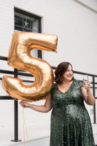 Woman in a sparkly green dress holding a large gold 5 balloon and a glass of champagne
