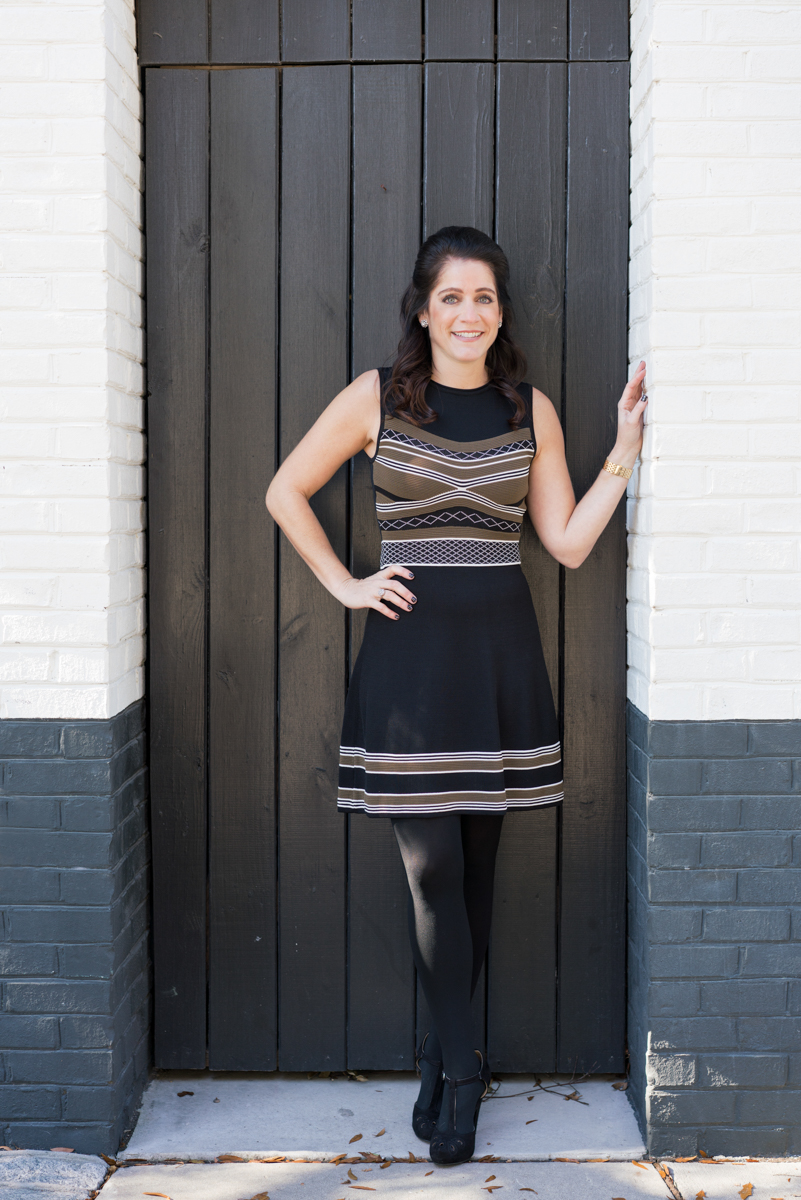 Woman in black dress with stripes posing with her hand against a wall