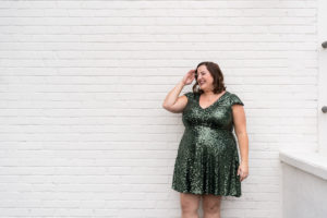 Woman in green sparkly dress standing against a white wall laughing