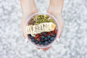 Two hands holding an acai bowl with bananas, pepitas, and blueberries