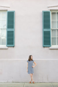 Woman in navy and white striped dress in front of a pink house with teal shutters