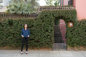Woman standing in front of a brick wall covered in ivy with an iron gate