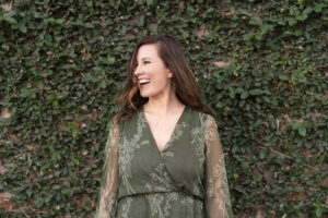 Woman entrepreneur standing against ivy wall smiling and laughing