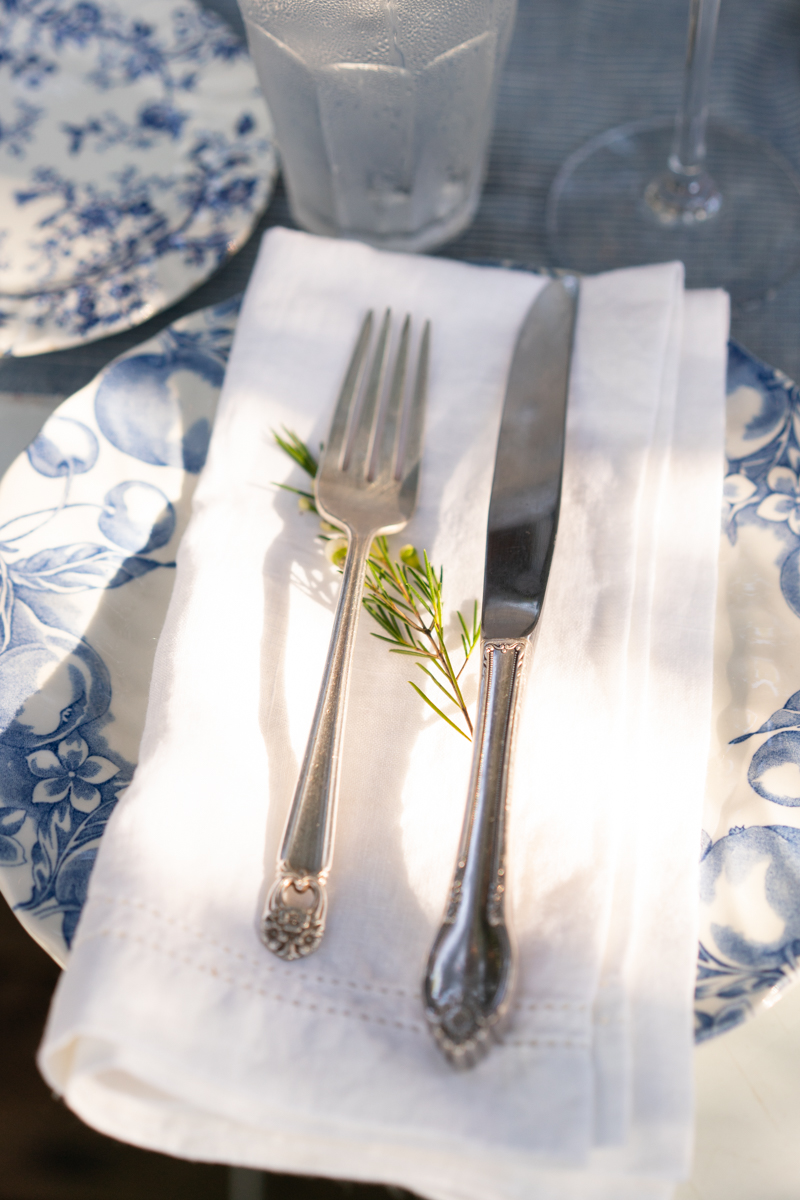 Fork and knife table setting on a blue plate, white napkin, and sprig