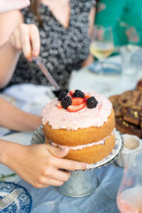 Women cutting into a vanilla cake with fruit on top