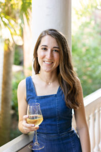 Woman holding a glass of white wine wearing a denim dress on a porch