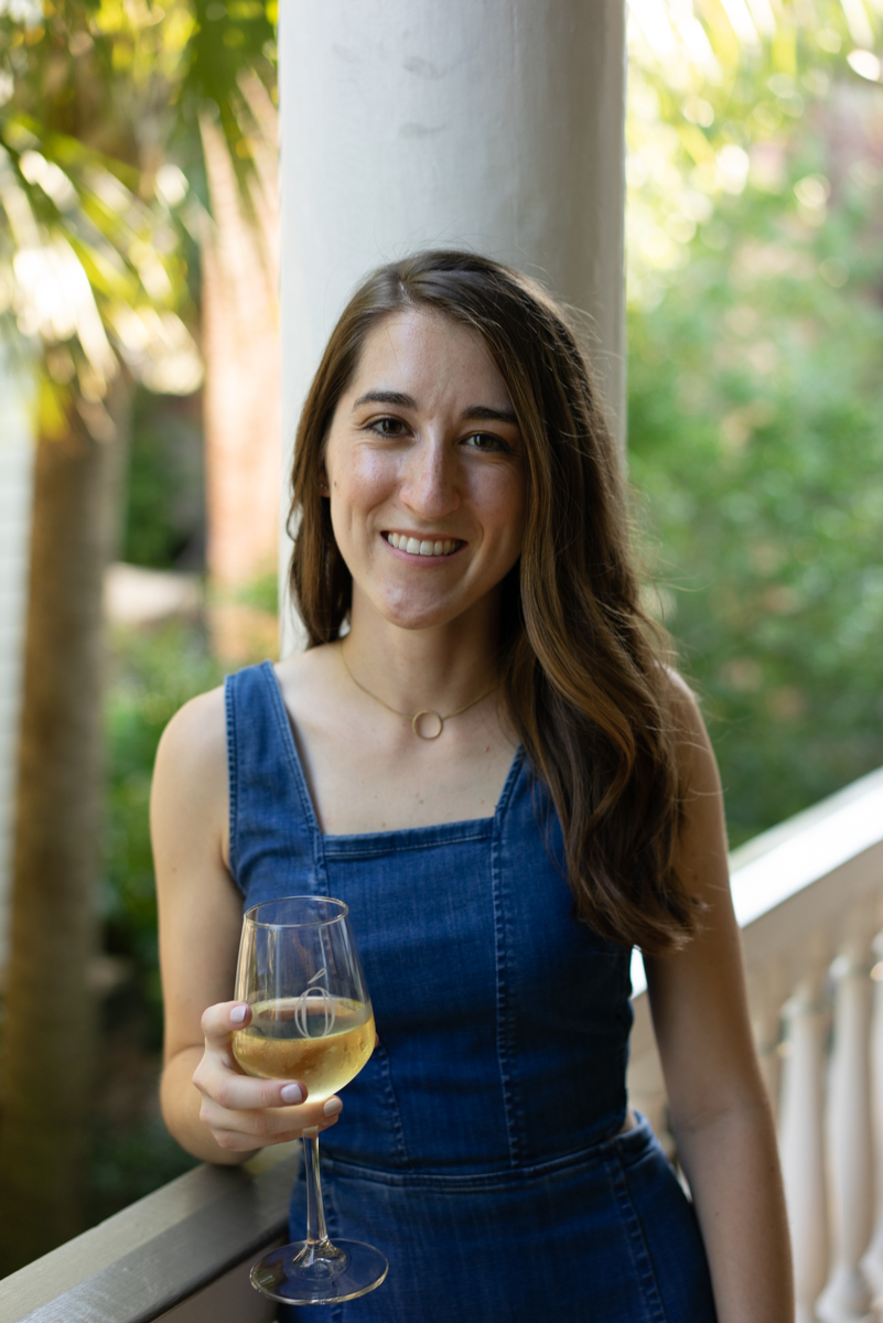 Woman holding a glass of white wine wearing a denim dress on a porch