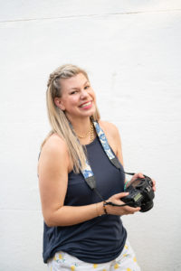Woman against a white background holding her camera and smiling at the camera