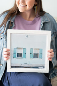 Woman holding a framed photo of a blue house in Charleston, SC