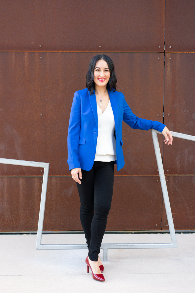 Woman in blue blazer and red heels standing against a red rust wall