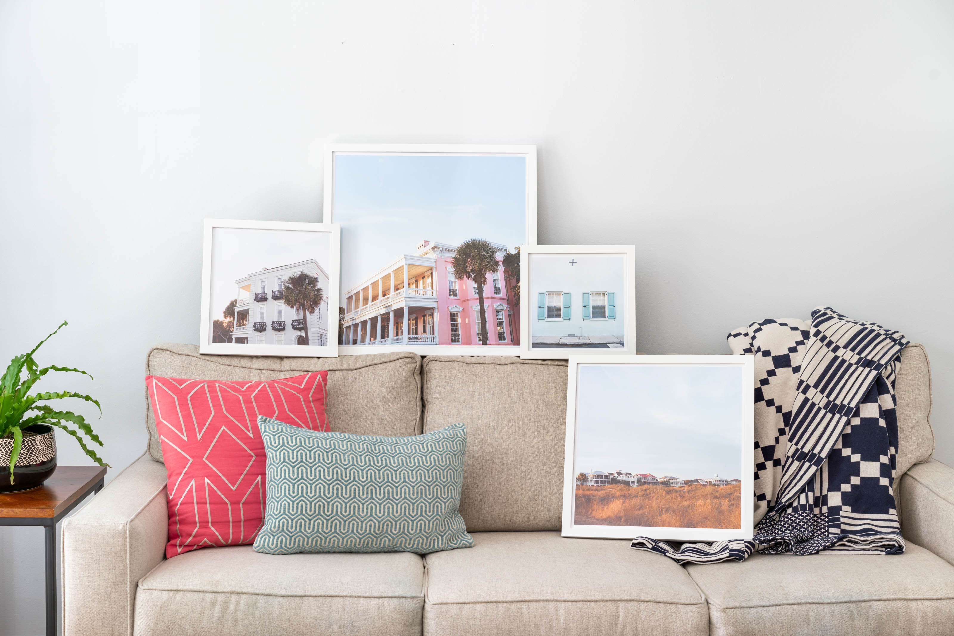 A collection of fine art photographs of Charleston, South Carolina in white frames sitting on a couch
