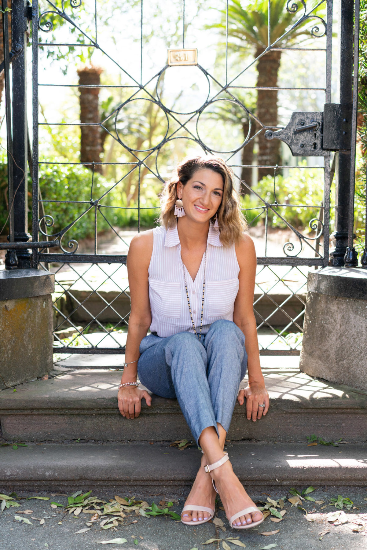 Portrait of a woman sitting on steps in front of an iron gate in Charleston, South Carolina. Her pose, leaning forward slightly with her ankles crossed, is an example of how to pose for brand photos. 