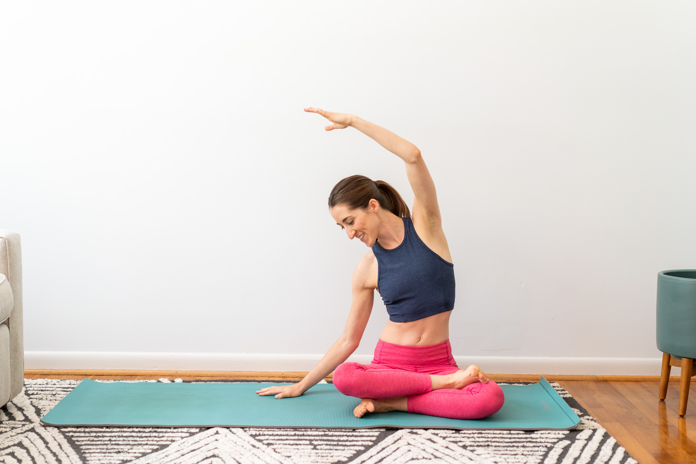 Woman sitting cross-legged on a blue yoga mat and doing a side stretch