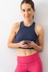 Woman wearing Outdoor Voices workout clothing holding an iPhone