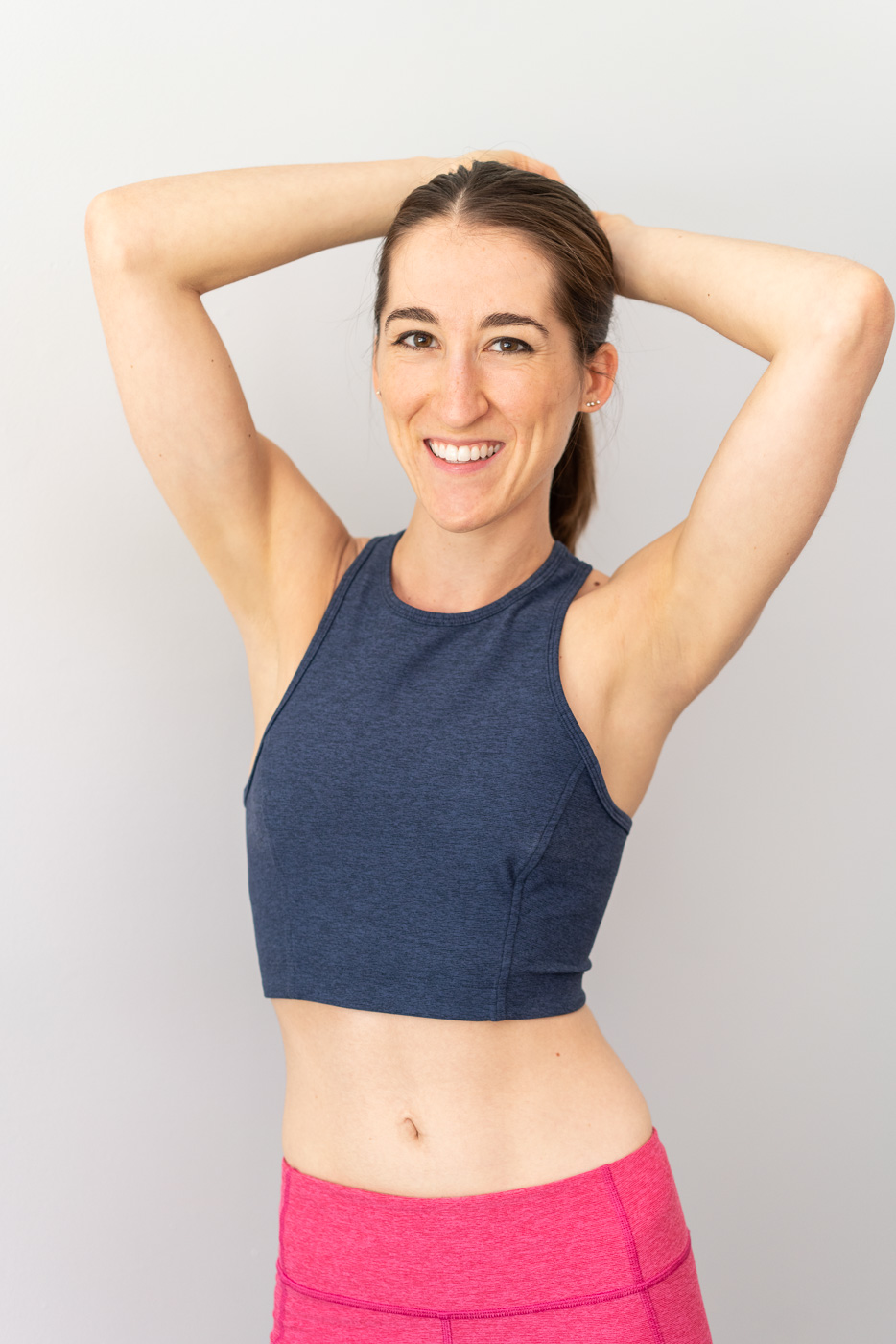 A woman in fitness clothing holding her hands behind her head and smiling