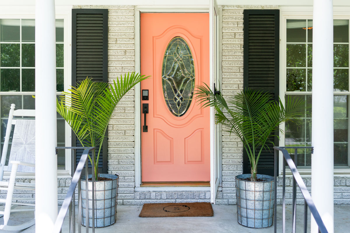 A bright coral front door with two planters filled with palms