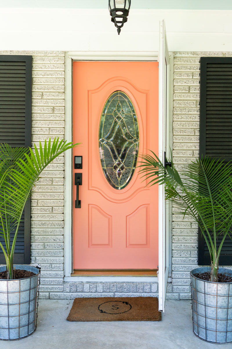 How to update your front door: A brightly colored front door with a West Elm door mat and two palms in galvanized planters