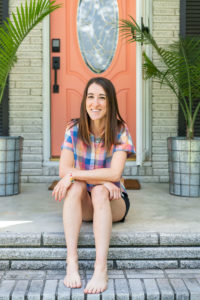Woman sitting on the steps of her house with a coral colored front door