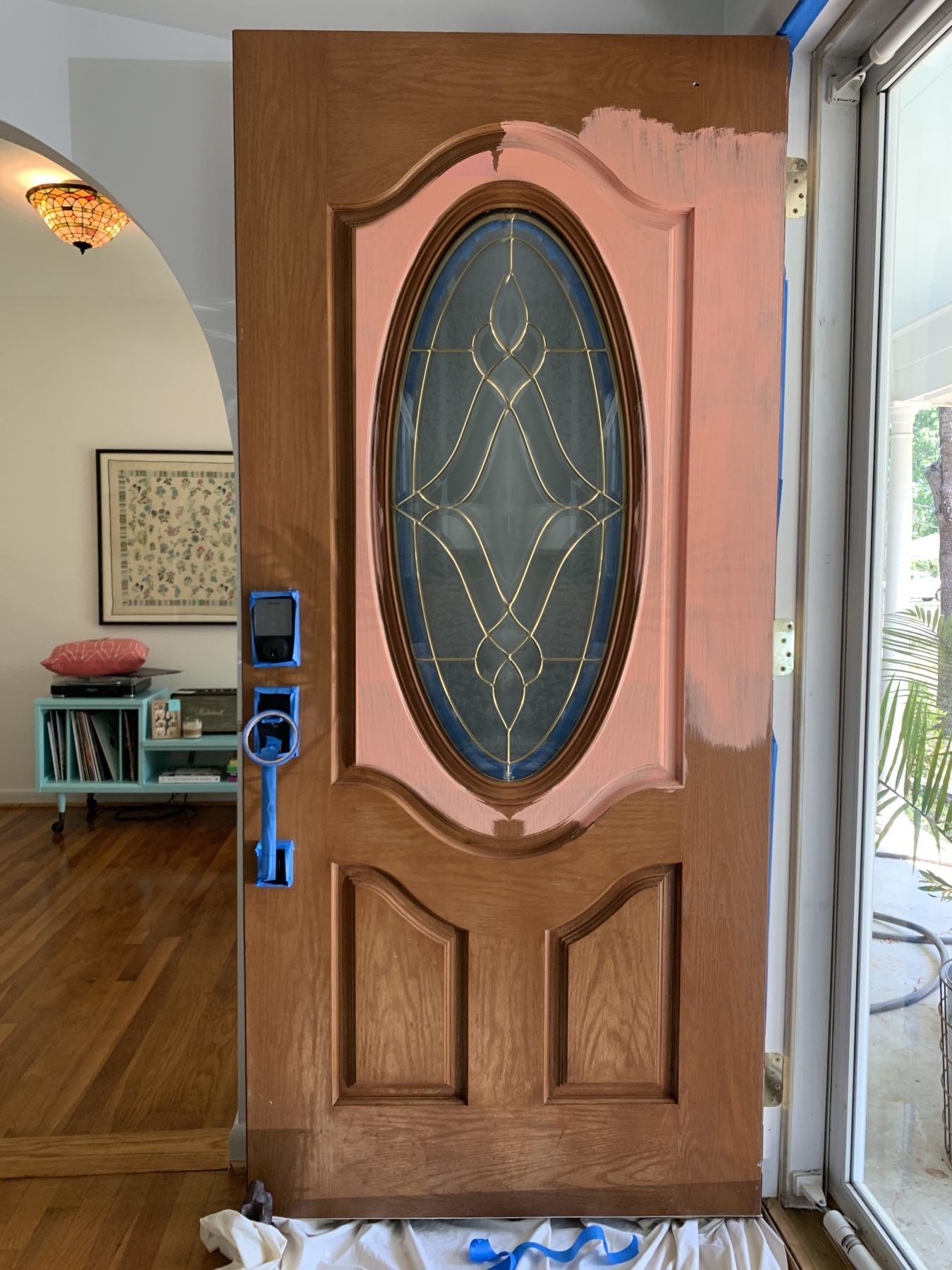 A brown wood front door in the process of being painted coral pink