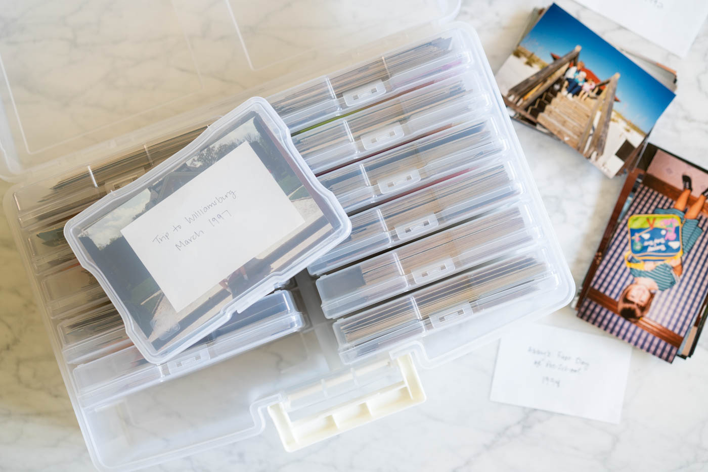 A clear plastic photo storage case surrounded by piles of 4x6" photos