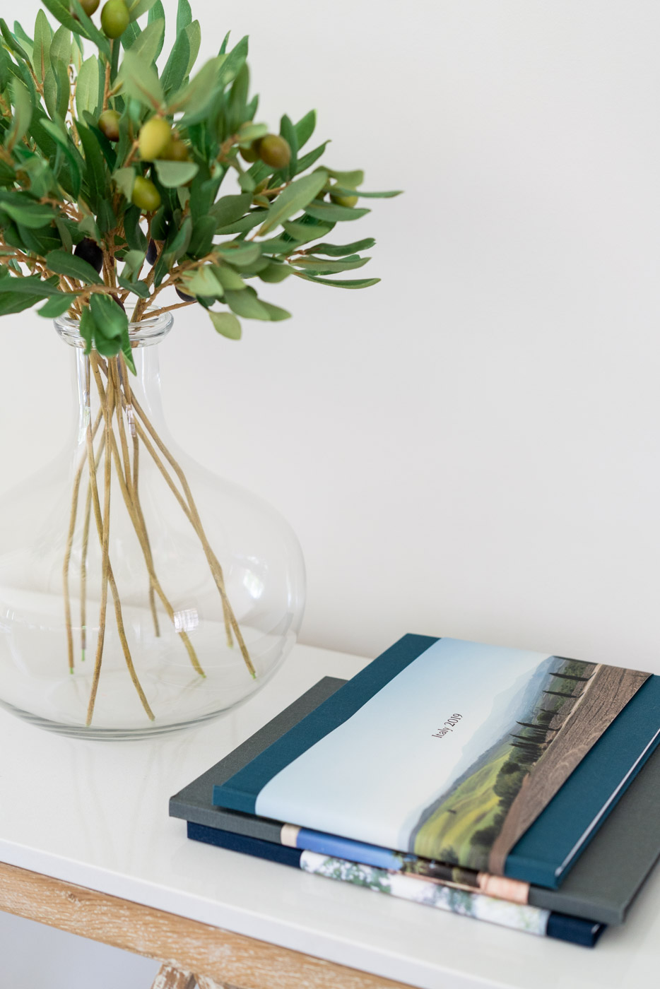 A stack of photo books next to a decorative vase with olive tree branches