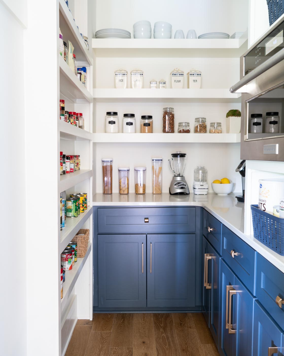 An organized kitchen pantry with white shelves and navy blue cabinets