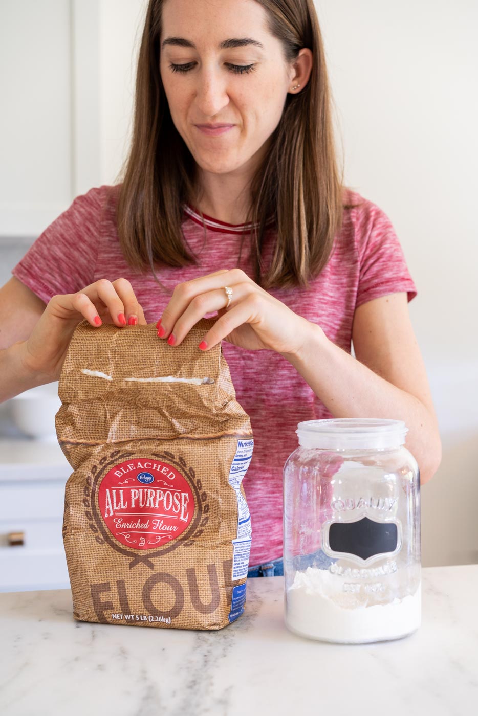Woman opening a bag of all purpose flour to transfer it to a glass container