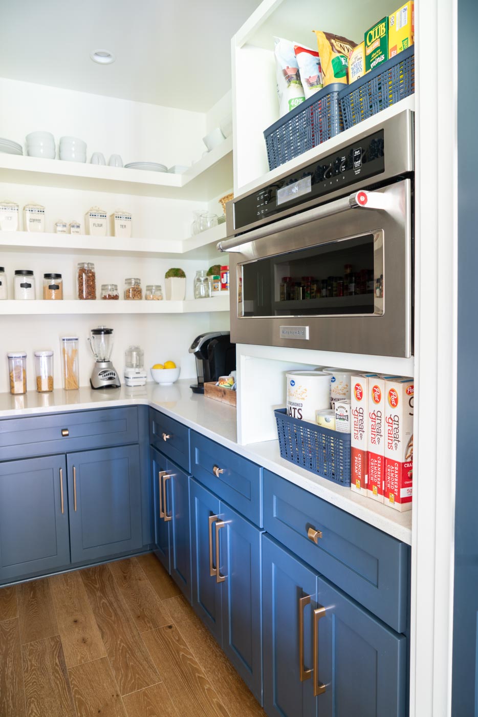 A organized kitchen pantry with a KitchenAid microwave and storage baskets and containers for pantry items