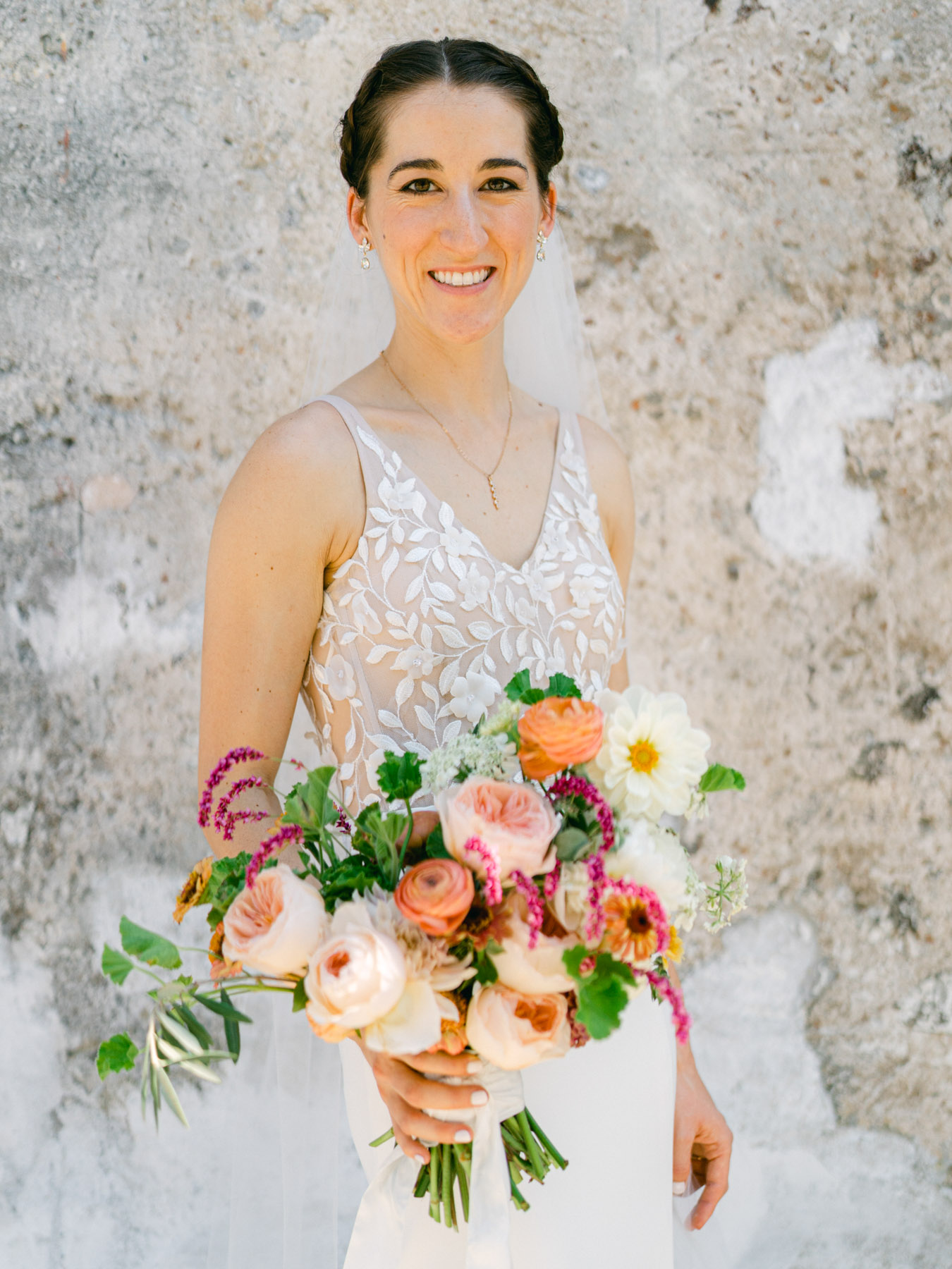 A bride with a braided updo posing with her brightly colored bouquet